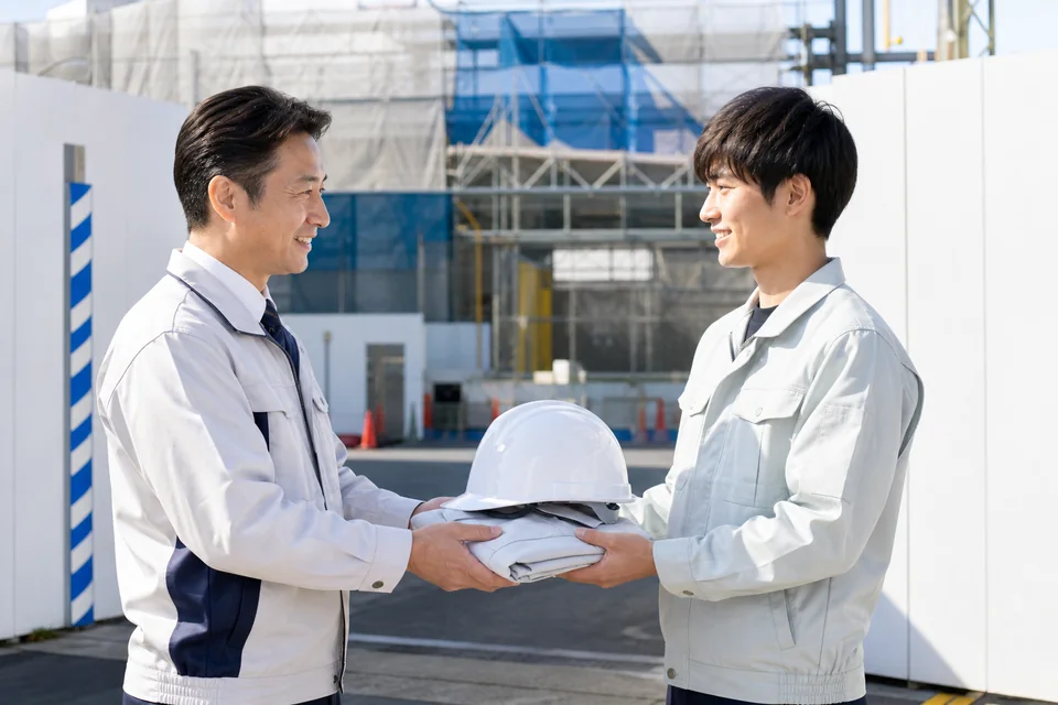 新入社員へヘルメットと作業着を手渡す現場責任者